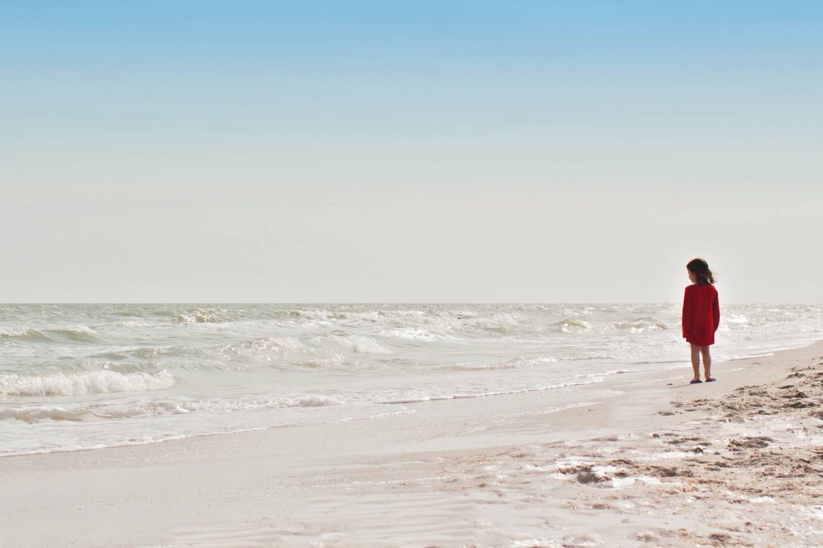 Child in red dress on beach looking out to sea