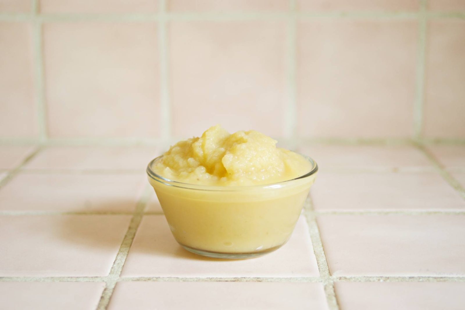 Glass bowl of yellow pureed food on light tiled background